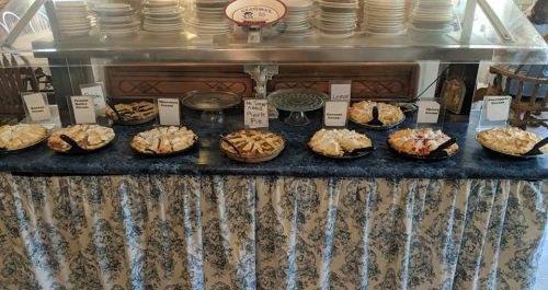 A dessert table featuring various pies, including apple, chocolate, and coconut, displayed on a blue tablecloth.