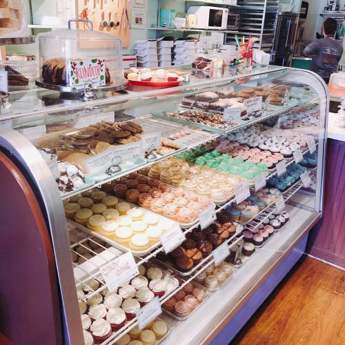 A display case filled with a variety of colorful baked goods, including cookies, cupcakes, and pastries.
