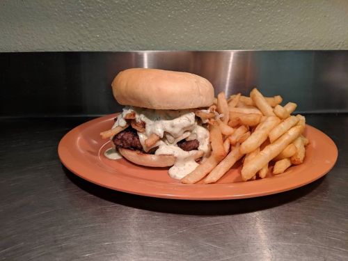 A juicy burger topped with creamy sauce and crispy onions, served with a side of golden French fries on an orange plate.