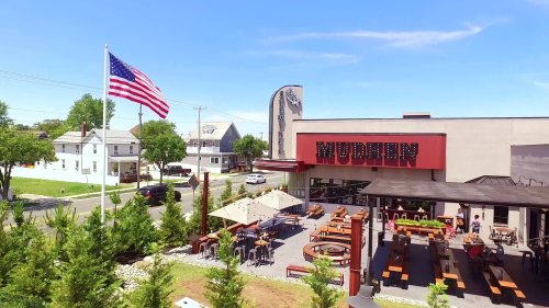 Aerial view of a restaurant named "MUDHEN" with outdoor seating and an American flag waving in the foreground.