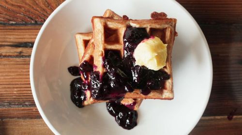 A plate of waffles topped with blueberry sauce and a dollop of butter, set on a wooden table.