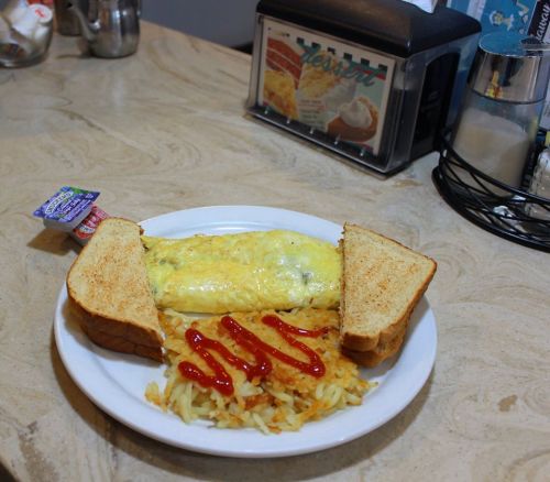 A plate with an omelette, hash browns, and two slices of toast with ketchup on the side.