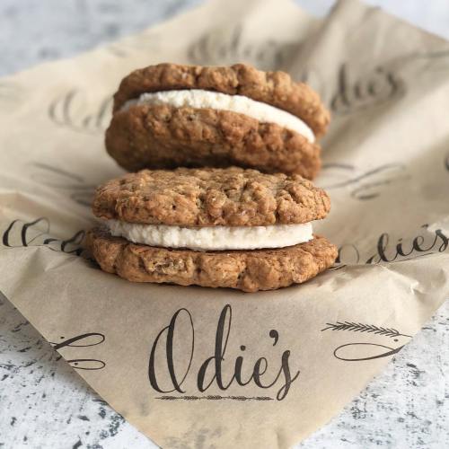 Two oatmeal cookies with cream filling stacked on a branded paper featuring the name "Odie's."