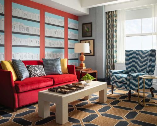 A stylish living room featuring a red sofa, patterned armchair, coffee table, and colorful wall decor.
