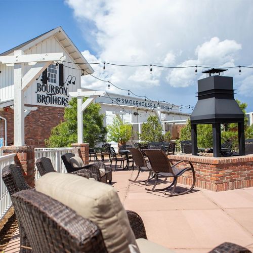 Outdoor patio with seating, string lights, and a fireplace, featuring the Bourbon Brothers Smokehouse & Brewery sign.