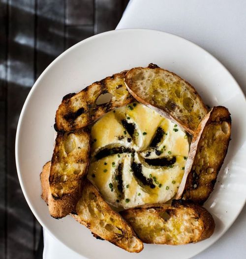 A plate of baked cheese surrounded by toasted bread slices, garnished with herbs.