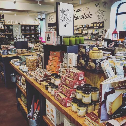 A cozy store display featuring shelves of gourmet foods, snacks, and cookbooks in a warm, inviting atmosphere.