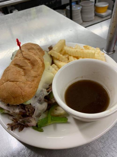 A plate with a sandwich filled with beef, peppers, and cheese, served with crinkle fries and a small bowl of gravy.