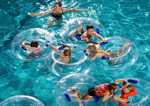 Children and a woman play in a pool with clear inner tubes, enjoying a sunny day.