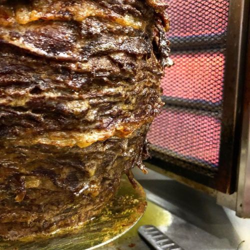 Close-up of a rotating vertical spit of marinated meat, crispy and golden brown, cooking in a vertical grill.
