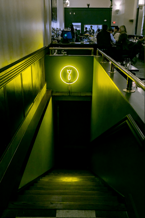 A dimly lit staircase leading down, illuminated by a green neon light in the shape of a wine glass.