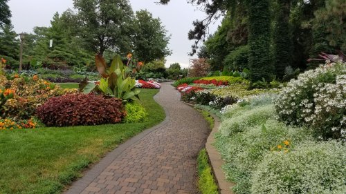 A winding path through a vibrant garden filled with colorful flowers and lush greenery on a cloudy day.