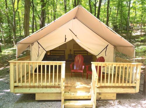 A spacious glamping tent with a wooden deck and red chairs, surrounded by trees in a forested area.