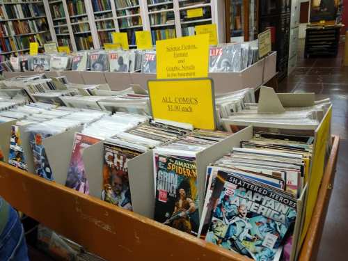 A display of comic books in a store, with signs indicating prices and genres like science fiction and fantasy.