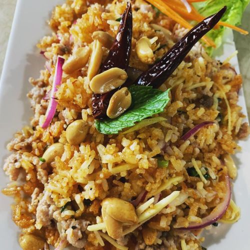 A plate of fried rice topped with peanuts, dried chilies, and fresh herbs, garnished with carrot and lettuce.
