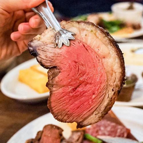 A hand holding a slice of medium-rare roast beef with a fork, showcasing its pink interior and crispy edge.