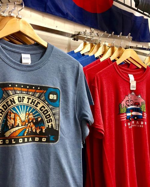 A display of colorful t-shirts featuring Colorado-themed designs, hanging on wooden hangers.