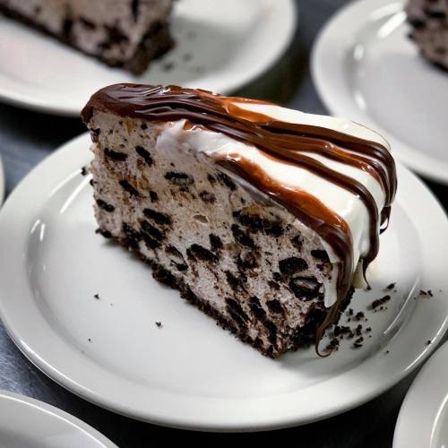 A slice of chocolate and cookie ice cream cake drizzled with chocolate and caramel sauce on a white plate.