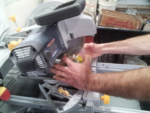 A person using a saw to cut colorful objects, with hands positioned near the blade and sawdust visible.