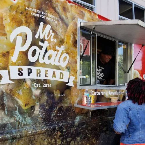 A food truck named "Mr. Potato Spread" with a customer ordering at the window. Catering options are advertised.