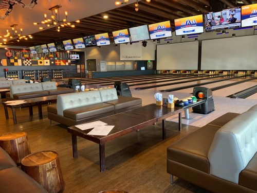 A bowling alley interior featuring lanes, seating areas, and multiple screens displaying scores and games.
