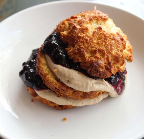 A biscuit sandwich filled with creamy filling and berry jam, served on a white plate.