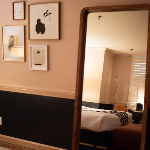 A stylish room featuring a mirror, framed art on the wall, and a cozy bed with modern decor.