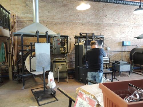A person works in a workshop with large machinery and equipment against a brick wall.