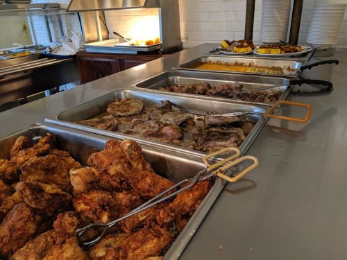 A buffet spread featuring various dishes, including fried chicken, meats, and sides in metal trays.