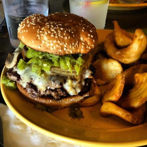A juicy burger with melted cheese, green peppers, and onions, served with crispy potato wedges on a yellow plate.