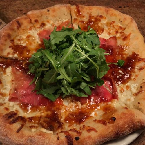 A pizza topped with cheese, ham, and a generous mound of fresh arugula in the center.