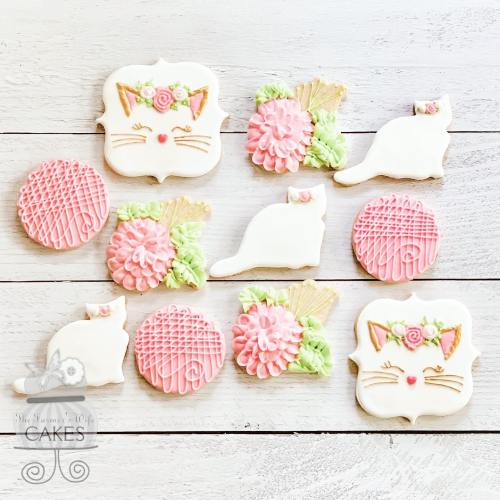 A variety of decorated cookies featuring cat shapes, flowers, and intricate designs in pink and green icing.