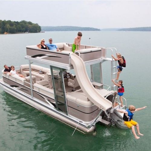 A family enjoys a fun day on a boat with a slide, kids playing, and adults relaxing on a sunny lake.