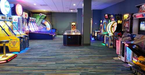 A brightly lit arcade with various games and machines lining the walls, featuring colorful lights and a vibrant atmosphere.