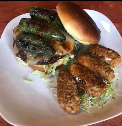 A burger topped with grilled jalapeños on a bun, served with crispy fried appetizers on a bed of sprouts.