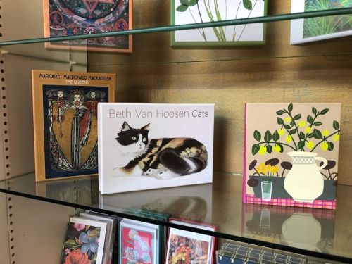 A shelf displaying books, including "Beth Van Hoesen Cats" and "The Queens," alongside a floral card.