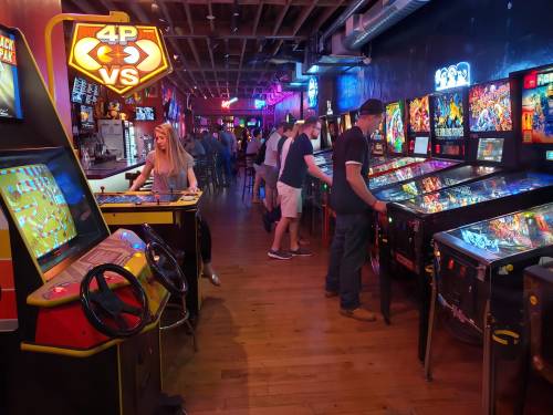 A lively arcade with vintage games, pinball machines, and people enjoying their time in a vibrant atmosphere.