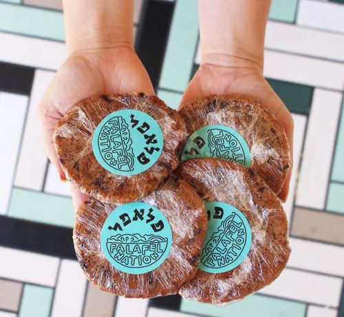 A pair of hands holding four wrapped falafel patties with a blue label reading "Falafel Nations."
