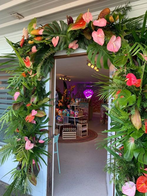 A vibrant entrance adorned with tropical plants and flowers, leading into a colorful, decorated interior space.