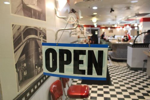 A large "OPEN" sign hangs in a diner with a checkered floor and vintage decor.