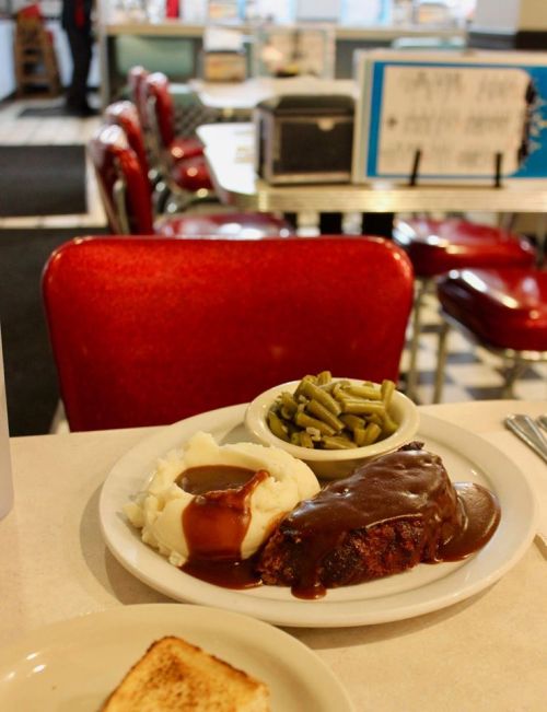 A plate of meatloaf with gravy, mashed potatoes, green beans, and a slice of toast on a diner table.
