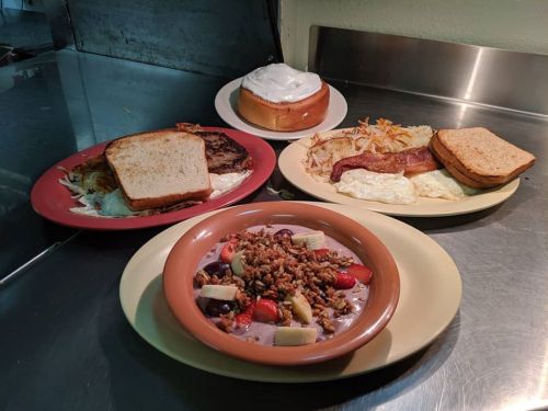 A variety of breakfast dishes: eggs, bacon, toast, hash browns, and a bowl of fruit with granola.