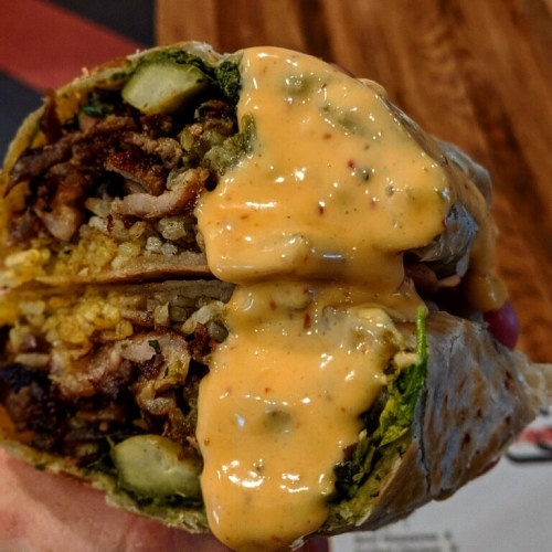 A close-up of a halved burrito filled with meat, rice, pickles, and drizzled with a creamy sauce.