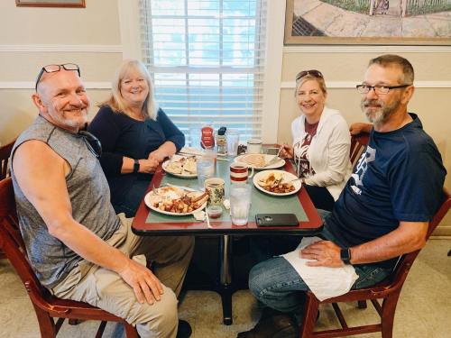 A group of four friends enjoying a meal together at a restaurant, smiling and seated around a table.