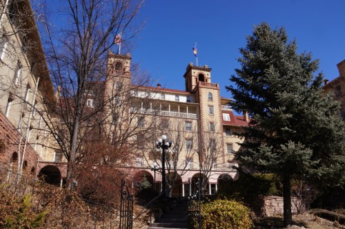 Historic building with towers, surrounded by trees and clear blue sky, featuring a flag on top.