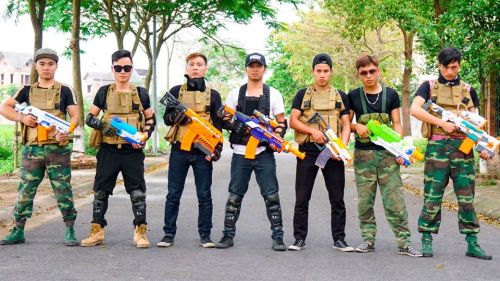 A group of six individuals in military-style outfits holding colorful toy guns, standing on a tree-lined street.