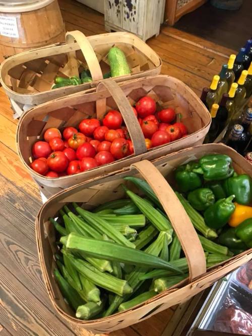 Three wooden baskets filled with fresh tomatoes, green bell peppers, and okra, displayed in a rustic setting.