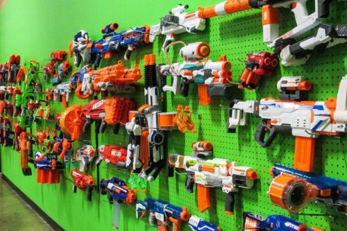A vibrant green wall displays a variety of colorful toy blasters and Nerf guns arranged neatly.