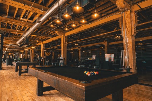 A spacious, stylish game room featuring a pool table, wooden beams, and warm lighting.