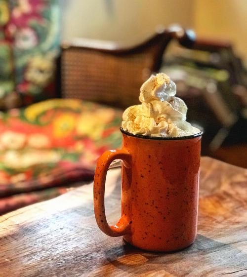 A cozy orange mug filled with a creamy beverage topped with whipped cream, set on a wooden table.